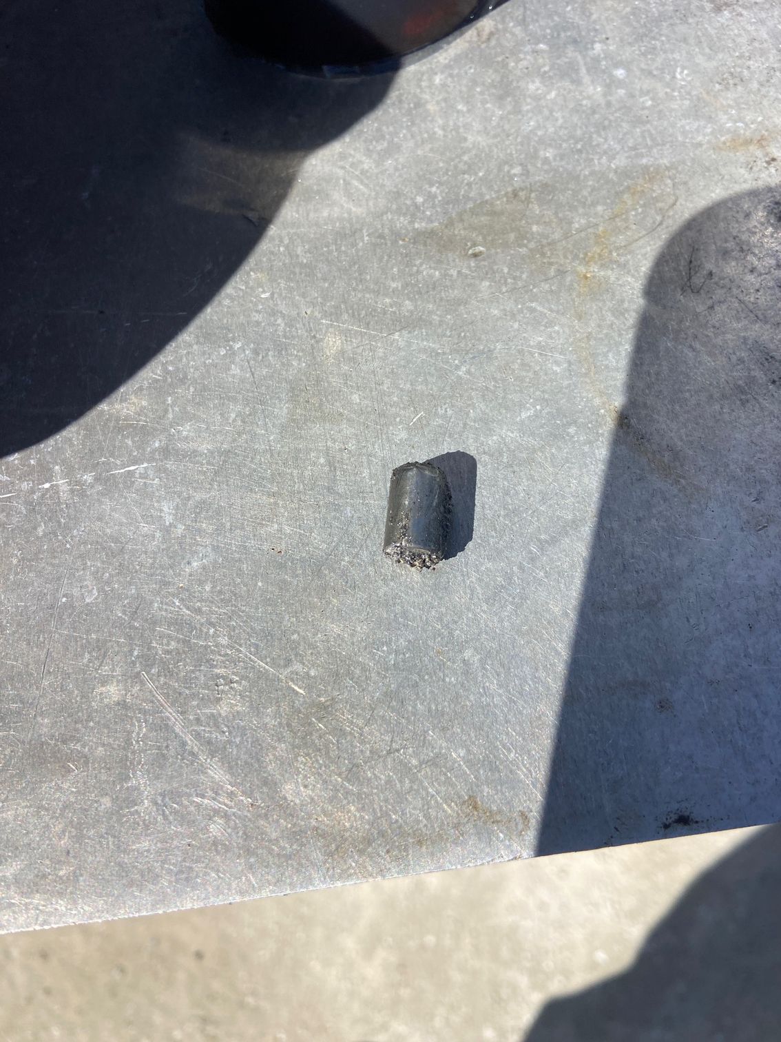 Small, dark, rectangular object on a light gray surface, possibly outdoors.