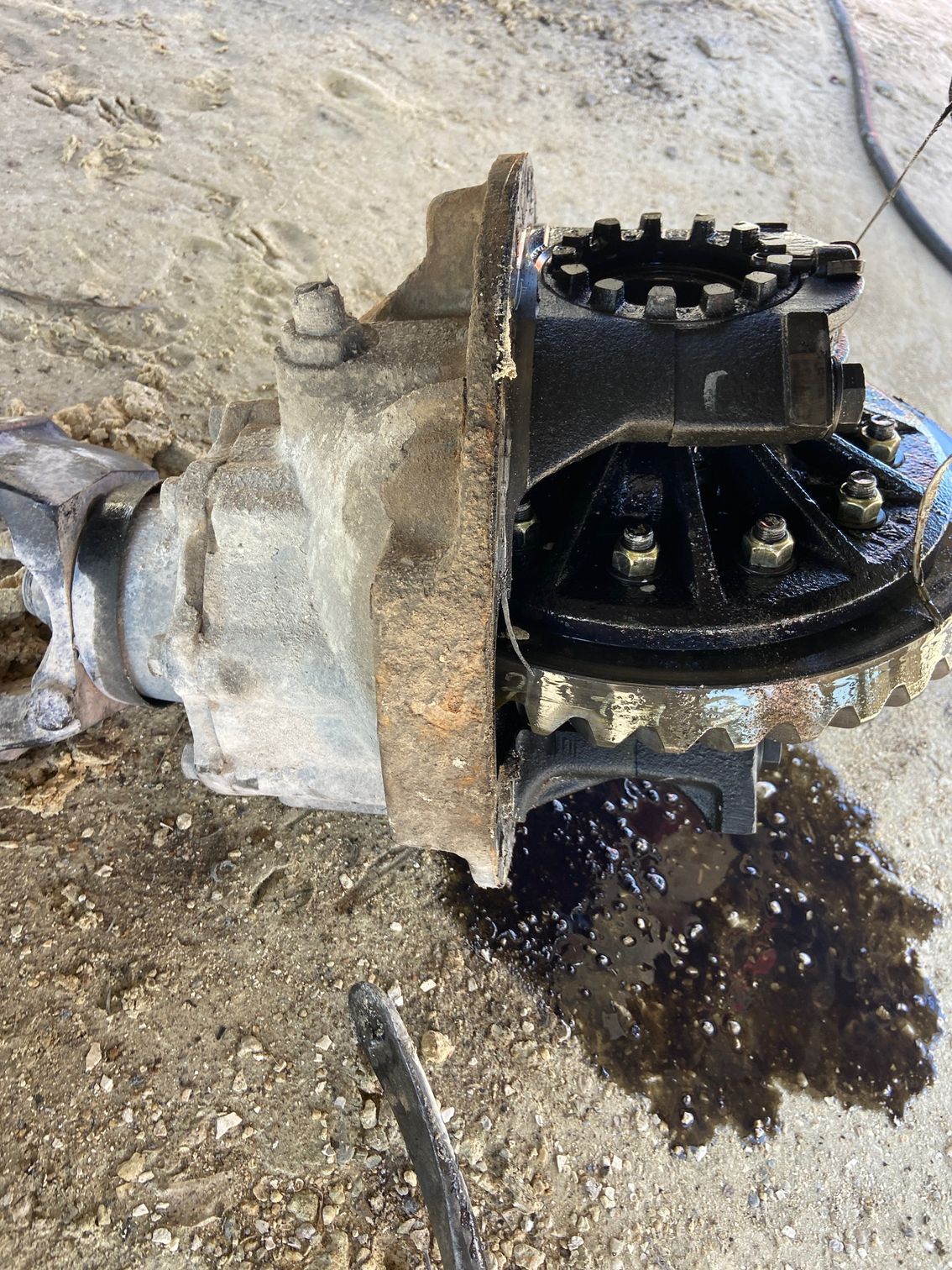 A disassembled car differential, with gear components visible, resting on a concrete surface. Oil is present.