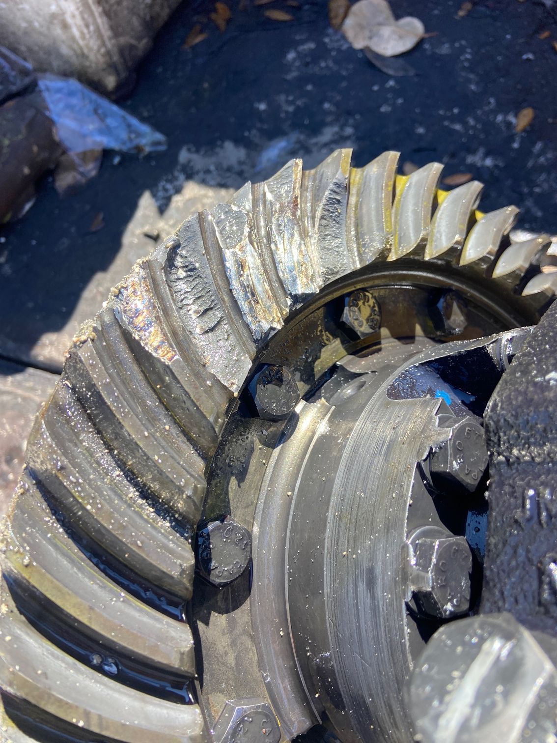 Damaged automotive ring gear with worn teeth, covered in oil and debris.