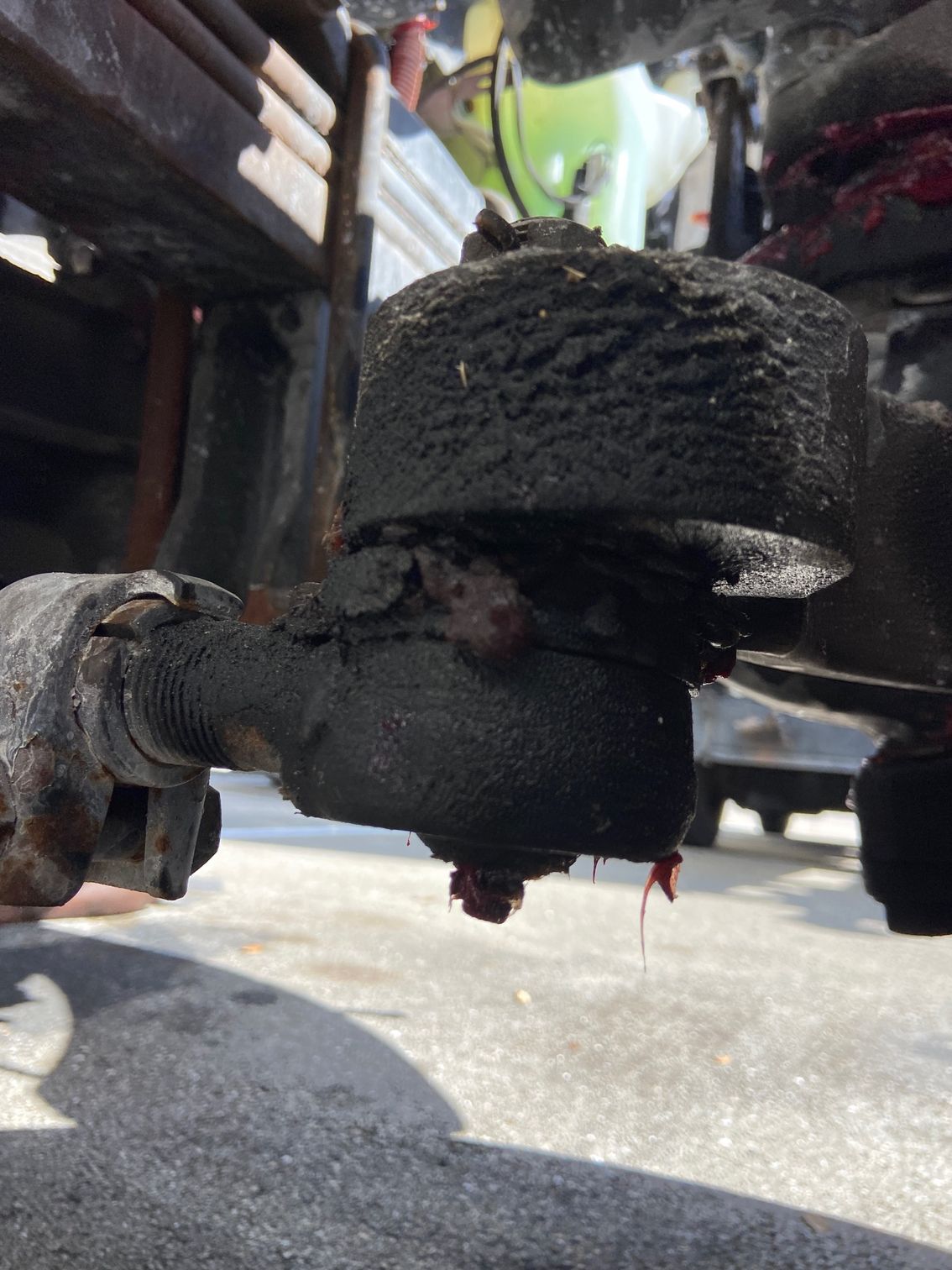 Close-up of a greasy, damaged ball joint on a vehicle's suspension system, with torn rubber boot and leaking grease.