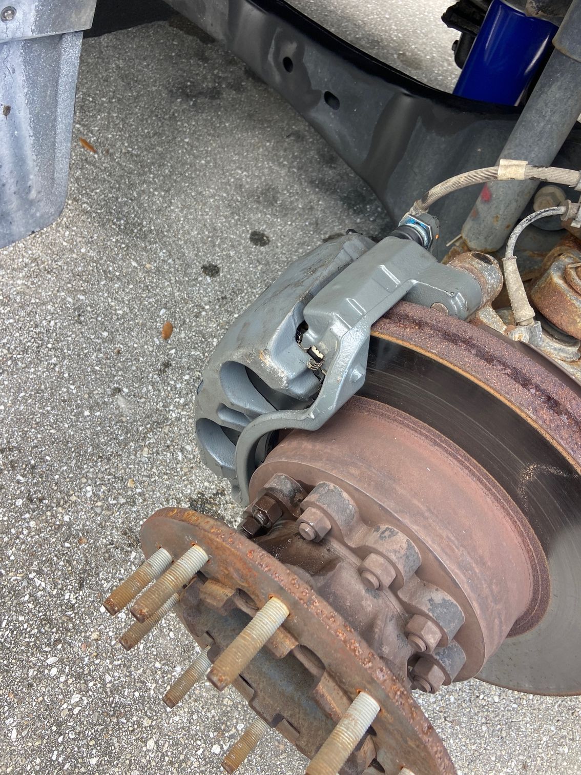 Gray brake caliper on a rusty rotor, attached to a vehicle's hub.