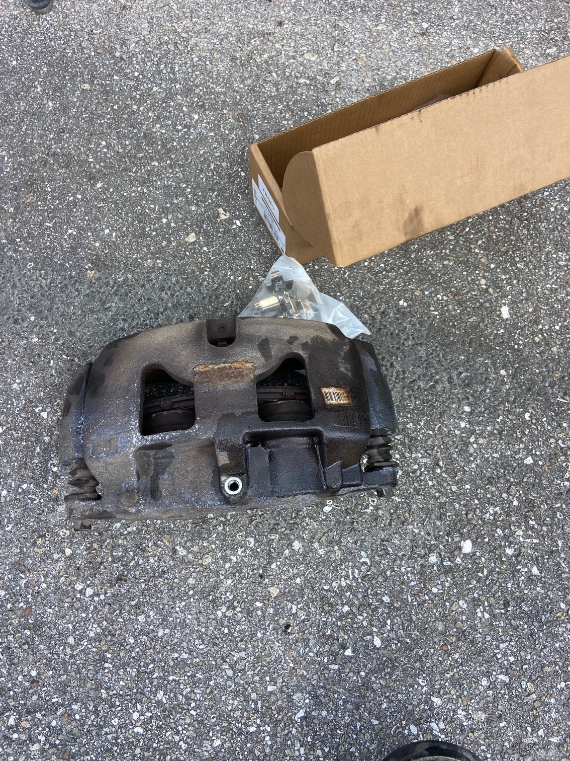 Black brake caliper with cardboard box on asphalt.