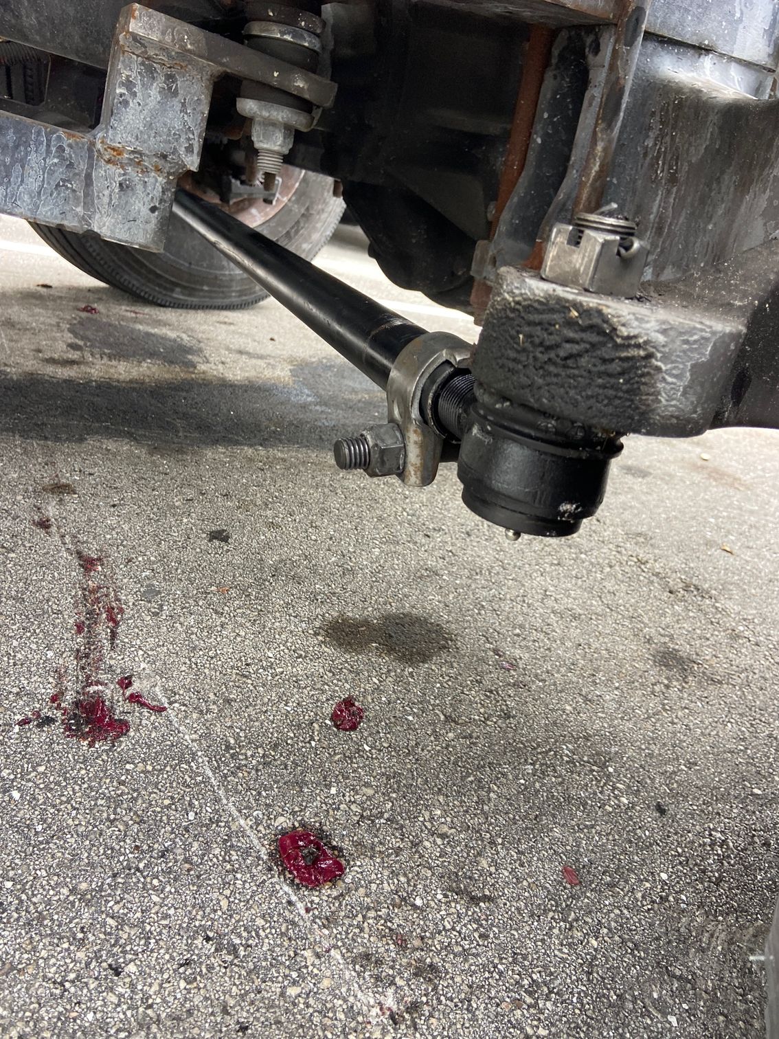 Truck's broken steering component with dark fluid puddles on pavement.