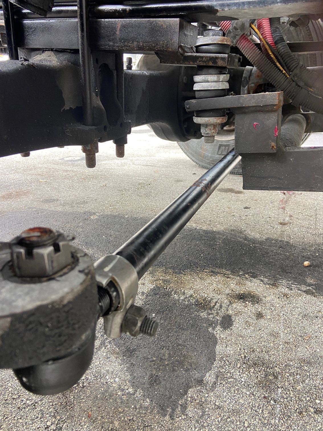 Undercarriage of a vehicle with a black drag link and associated suspension components, on asphalt.