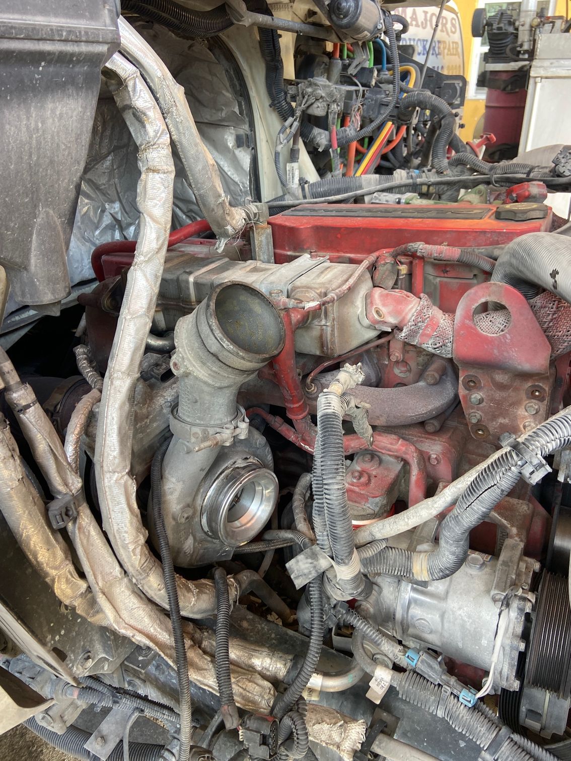 Engine compartment of a semi-truck with a turbocharger visible, red engine components, and wiring.