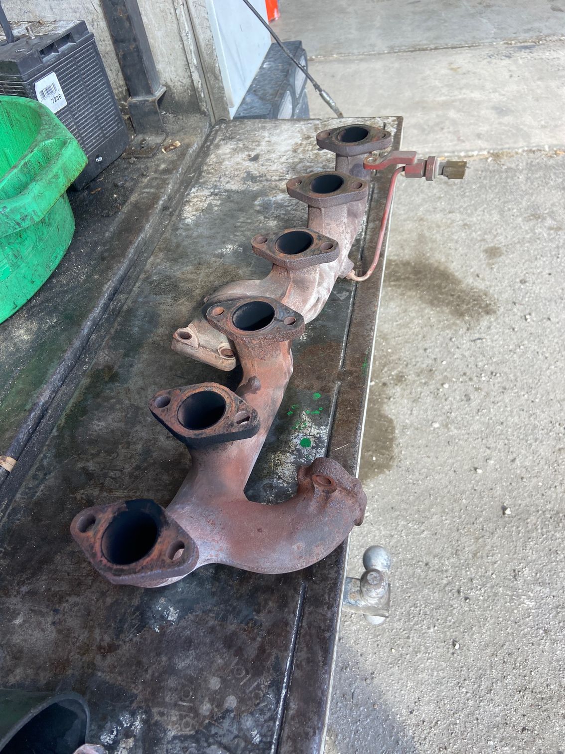 Rusty engine exhaust manifold on a work surface, showing six ports.