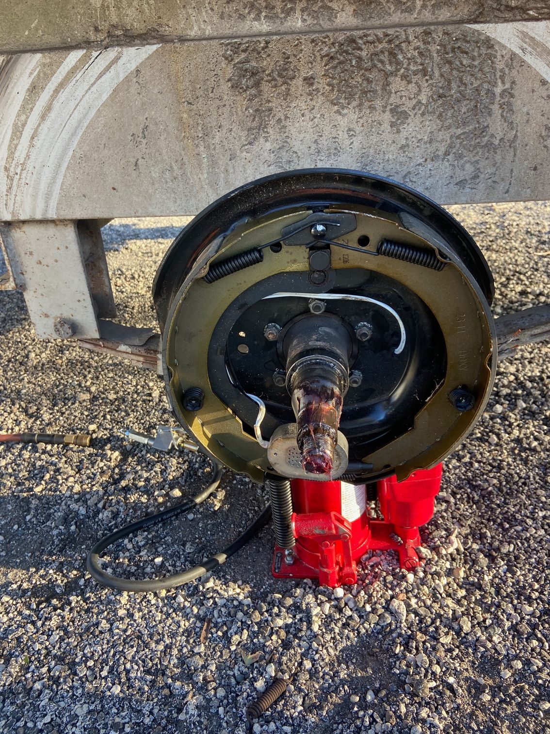 Trailer wheel assembly with exposed brake components, red jack, and a concrete setting.