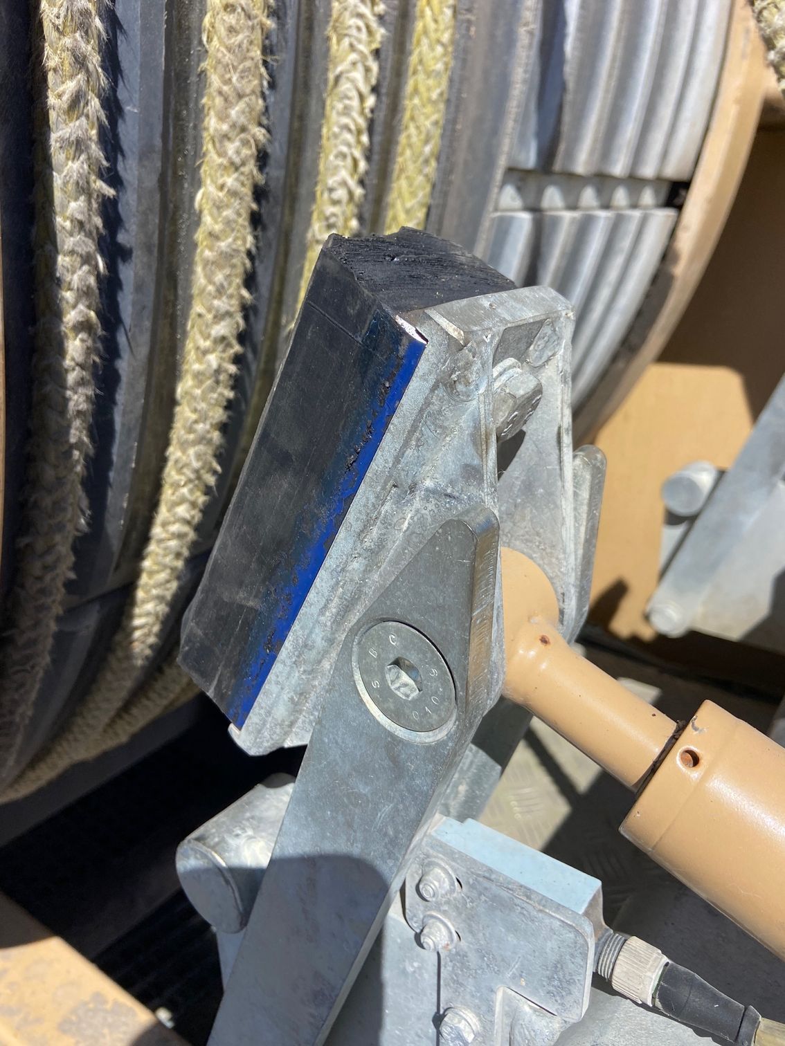 Metal cable spool with a silver-colored bracket holding a silver and blue block.