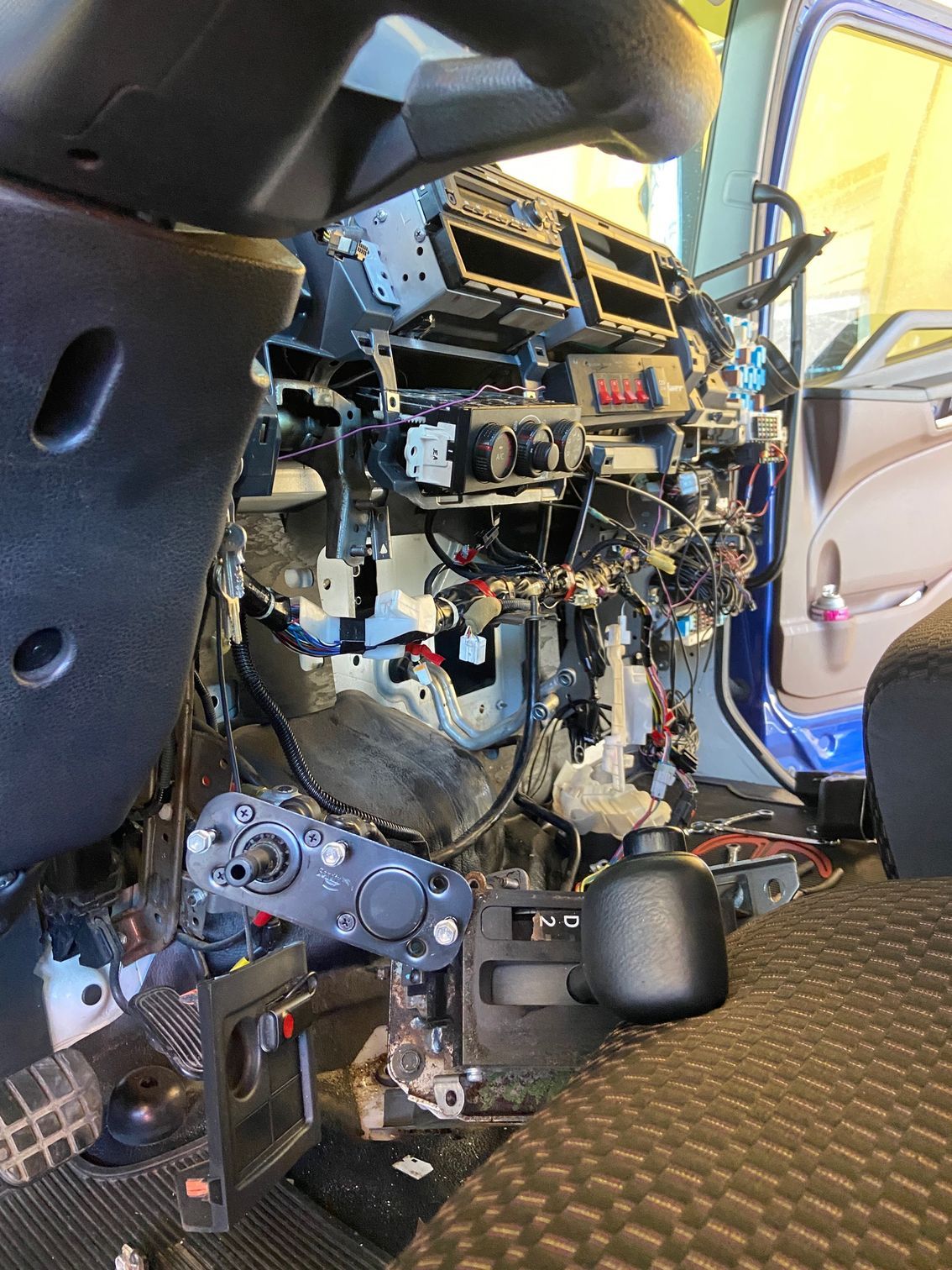 Interior view of a truck dashboard dismantled, showing wiring, controls, and components, with black and gray elements.