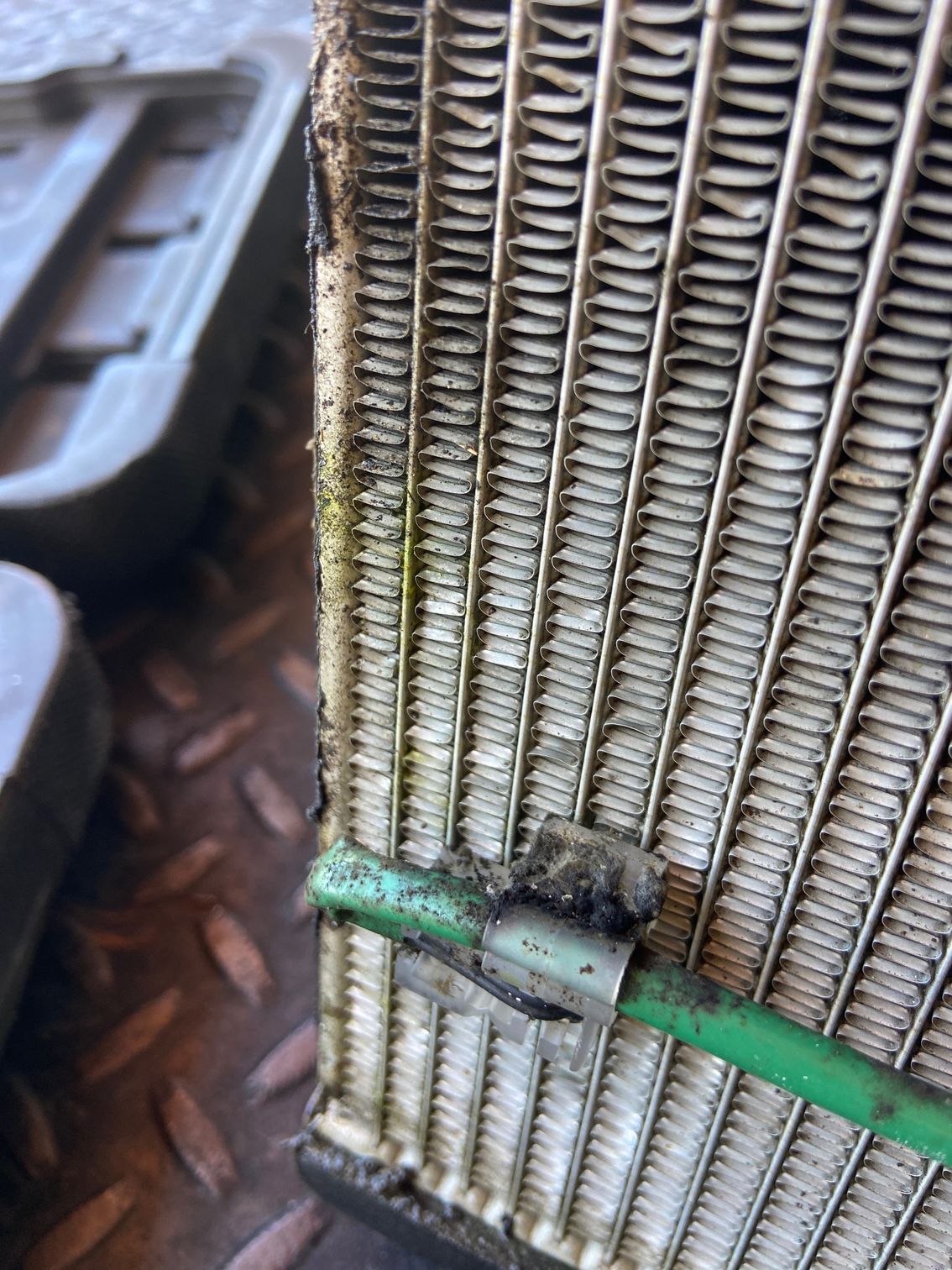 Close-up of a dirty automotive radiator with green tubing and a retaining clip.