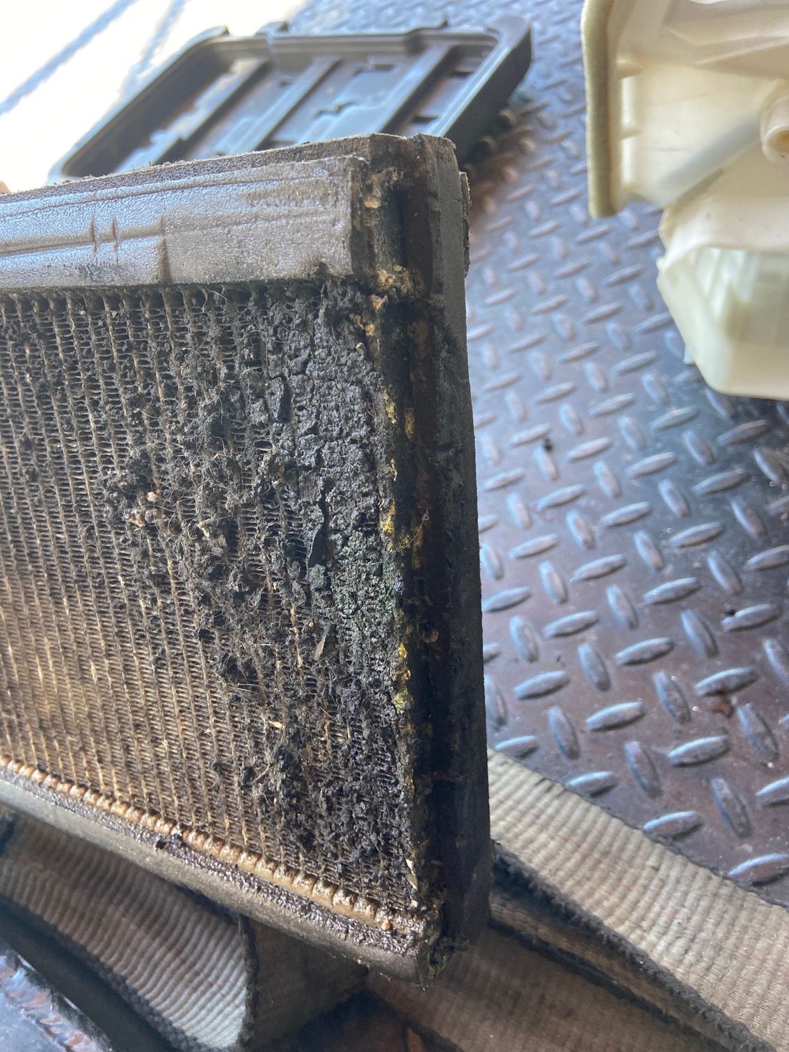 Dirty, clogged car air filter being removed. Black debris covers the filter's surface.