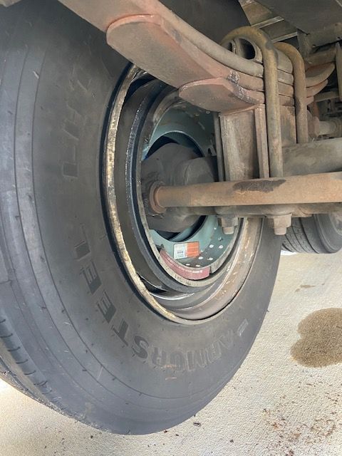 Close-up of a semi-truck tire and brake system, showing the wheel, tire tread, and brake drum. Brown fluid is visible.