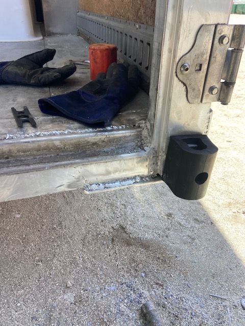 Metal frame with black component attached, gloves, and tools on concrete surface.