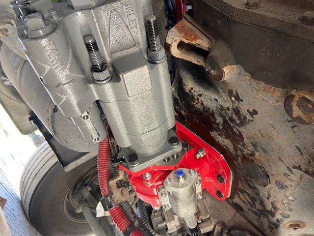 Undercarriage of a truck with a grey component bolted to a red bracket; exposed wires and a wheel are visible.