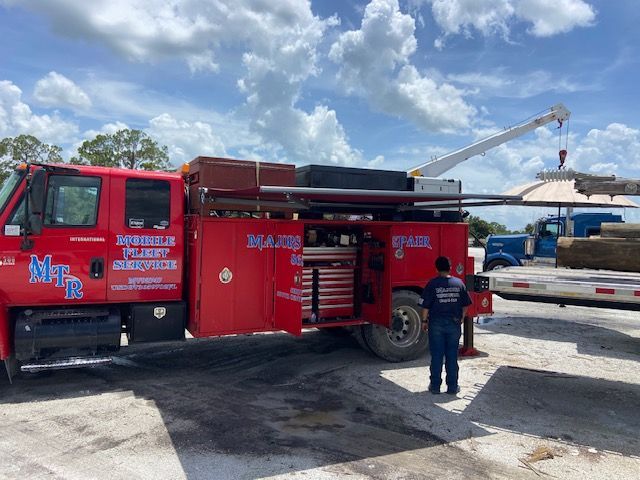 Red work truck with crane lifting a large round structure. A person stands nearby.