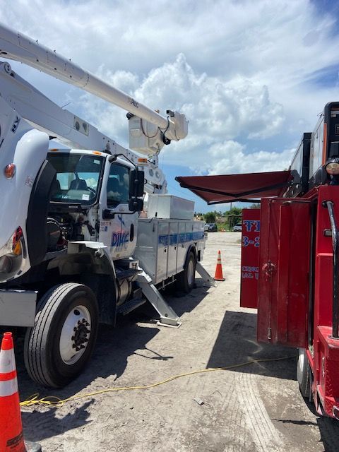 Utility truck with an extended boom, parked next to a red truck, under a cloudy sky.