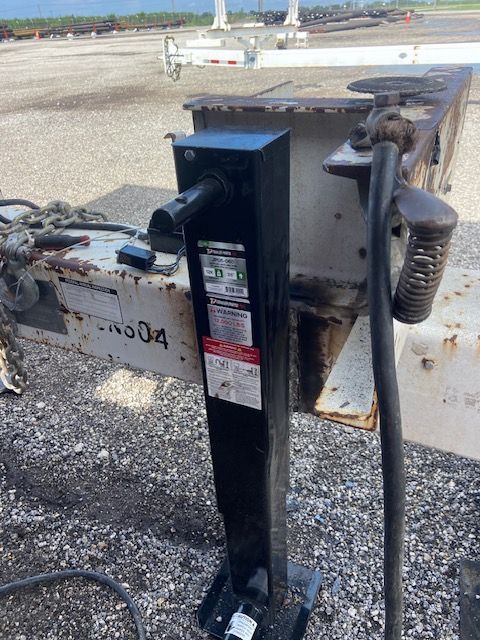 Black trailer jack on a white trailer; asphalt background.