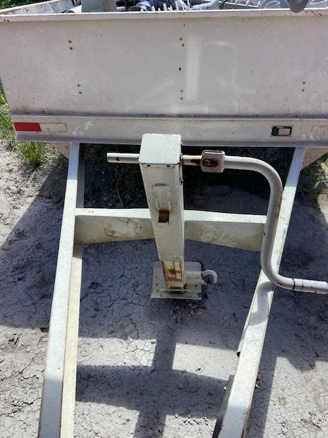 Silver trailer frame with a vertical jack and hand crank.