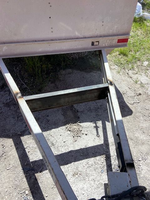 Metal trailer frame with welded supports, partially in shadow.