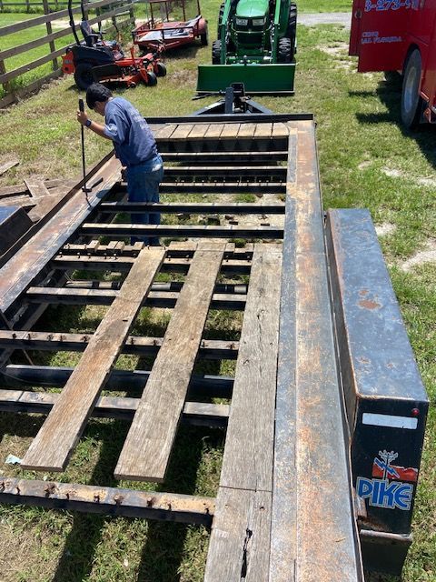 Man repairing a trailer, installing wood planks. Farm equipment visible in the background.
