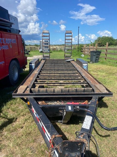 Black trailer with metal frame and ramps on green grass under a blue sky.