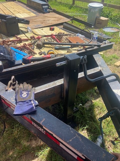 Tools and equipment on a black trailer bed, including a jack, wrenches, and welding gear outdoors.