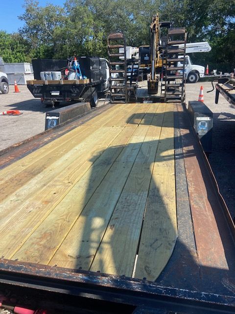 A flatbed trailer with new wooden planks. A vehicle and equipment sit on the trailer, outdoors.