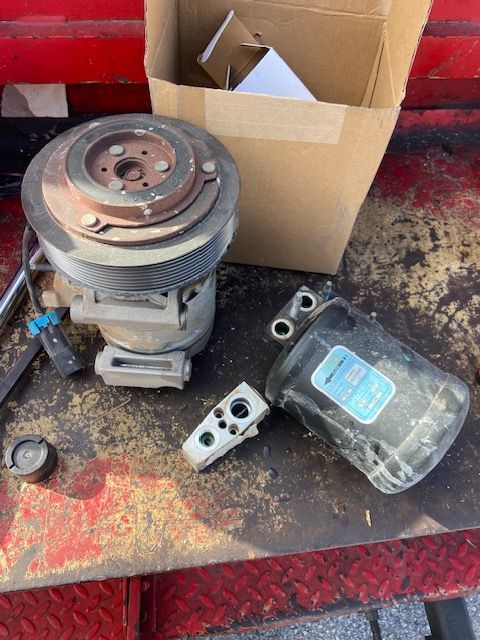 Car AC compressor and components on a rusty surface.