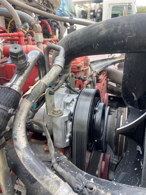 Close-up of a truck engine with an air conditioning compressor, hoses, and belt system visible.