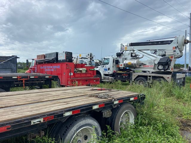 Trucks and heavy machinery parked outdoors with a cloudy sky.
