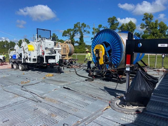 Construction site with machinery, a large blue cable reel, and workers on a metal platform under a blue sky.