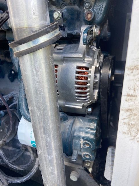 Silver alternator on a Kubota engine with a belt, near a metal pipe.