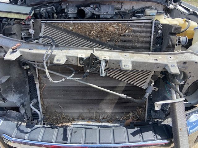 Front of a damaged car with exposed radiator and engine components. Debris and dirt visible.