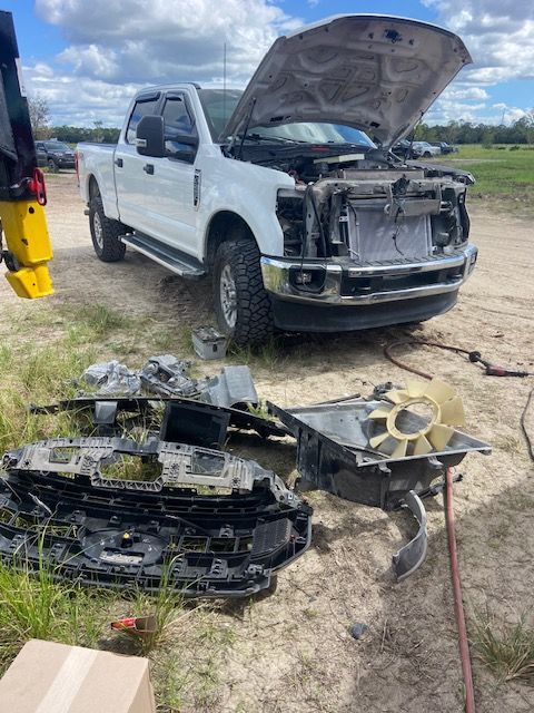 White truck with hood open, various parts scattered in front of it in a field.