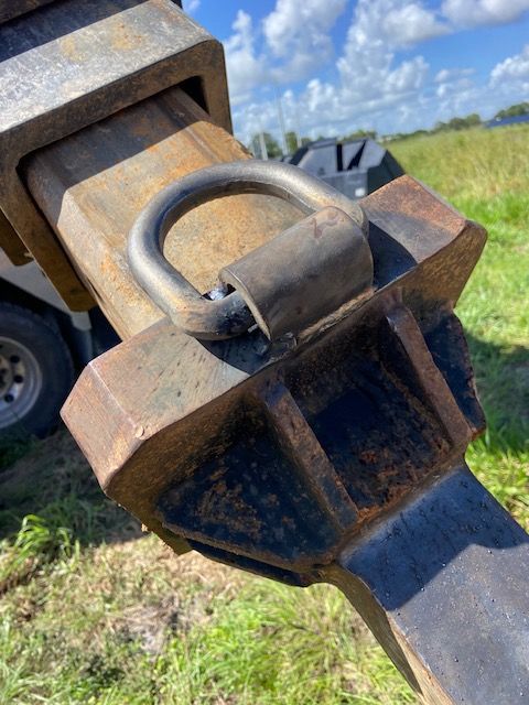 Close-up of a large, rusty metal hook with a D-ring attached, outdoors.