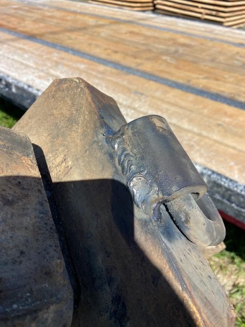 Close-up view of a dark metal weld on heavy machinery, against a blurred wooden surface.