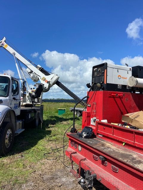 Truck with crane extending over a field, near another truck with a generator, under a blue sky.