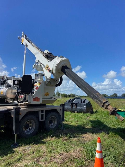 A truck-mounted drilling machine on a grassy field with a raised drill arm under a blue sky.