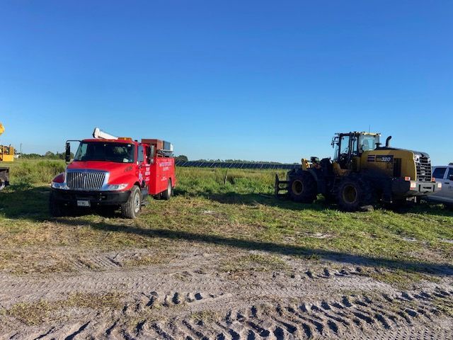 Red truck and yellow bulldozer parked on a grassy field under a clear blue sky.