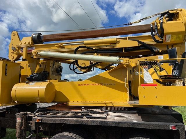 Yellow utility truck with raised boom against a cloudy sky.