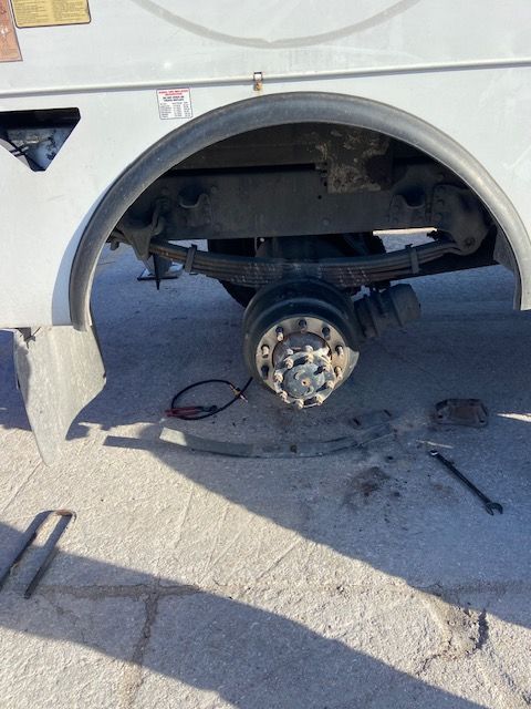 Rear axle of a white vehicle with a wheel removed, revealing suspension components, outdoors.