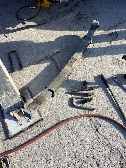 Metal suspension arm, tools, and a red hose lie on a concrete surface.