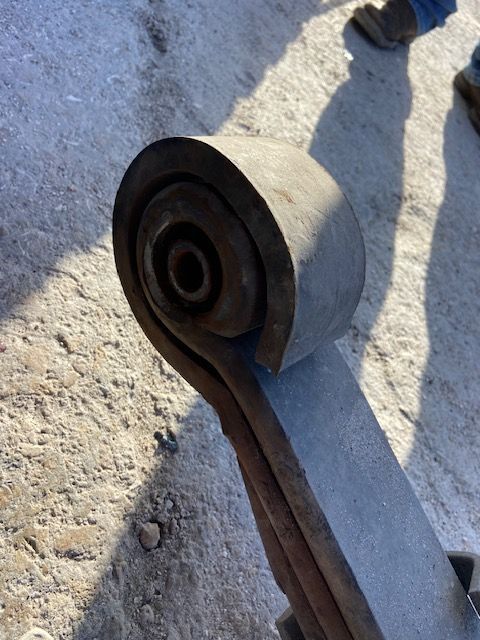 Leaf spring assembly with a rubber bushing, close-up shot on concrete.