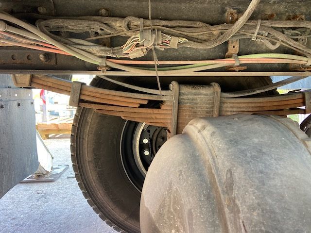 Undercarriage of a truck, showing rusty leaf spring above a tire. Wires and other components are visible.