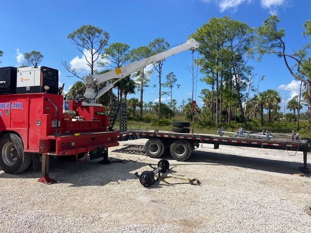 Red truck with crane next to a flatbed trailer in a sunny outdoor setting.