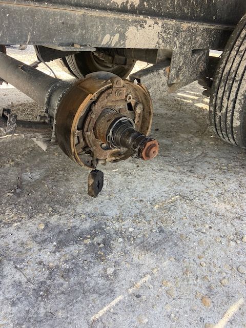 Truck axle with exposed brake components, resting on dirt ground.