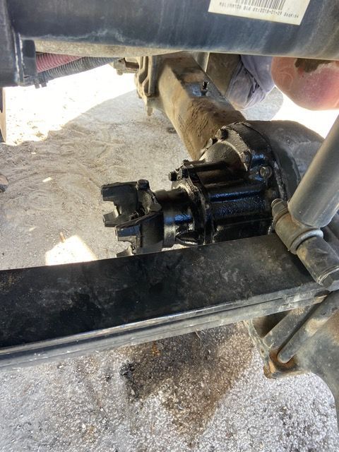 Black vehicle axle with exposed driveshaft connection, bolted to the suspension, outdoors.