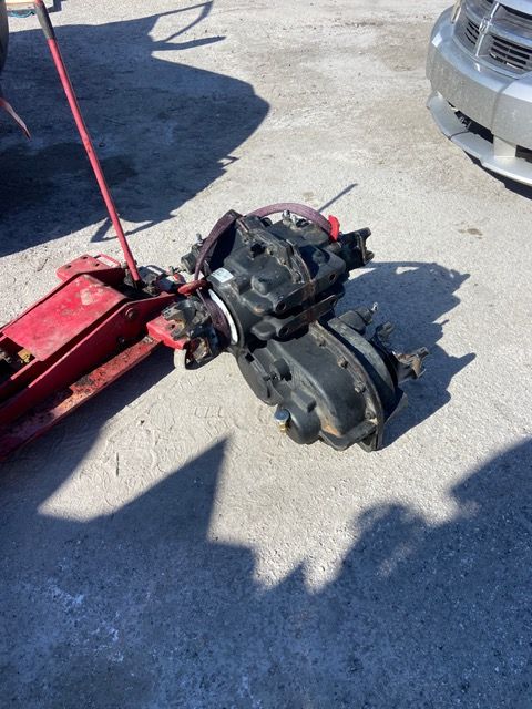 Black mechanical parts beside a red jack on a concrete surface.