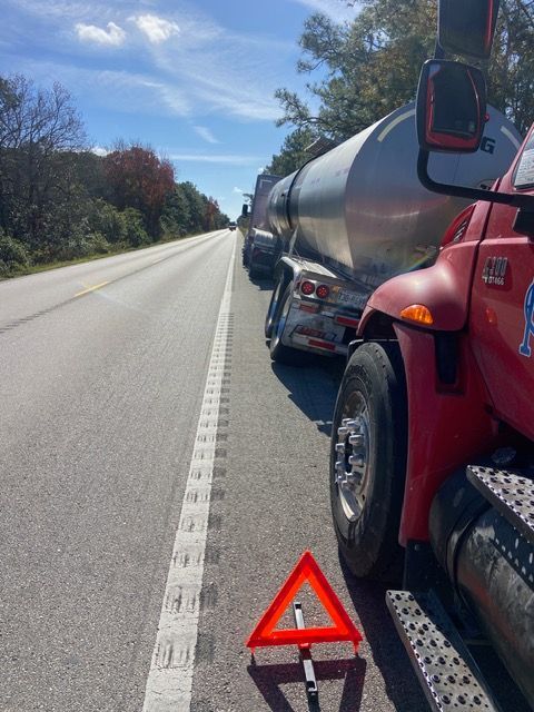 A red tanker truck is pulled over on the side of a road, with a warning triangle in front.