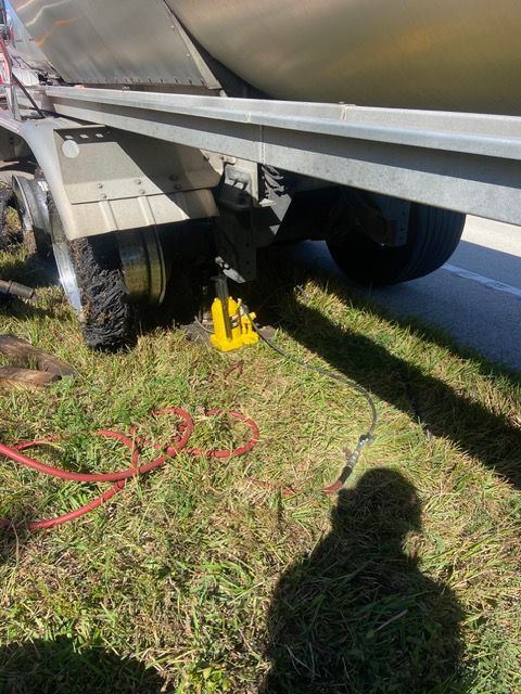 Yellow jack lifting a trailer wheel on grassy roadside. Red hose, shadow visible.